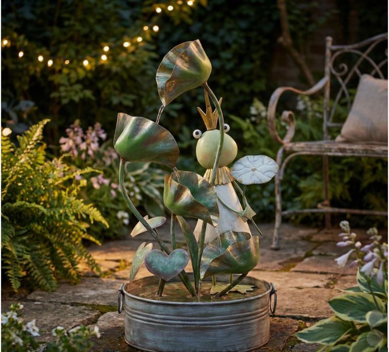 Metal fairy sculpture in a garden setting with plants and a bench.