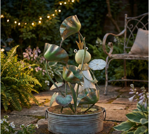 Metal fairy sculpture in a garden setting with plants and a bench.