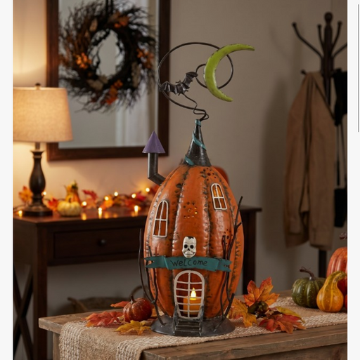 Decorative pumpkin house with candle on a table, surrounded by autumn leaves and pumpkins.