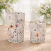 Two floral-patterned candle holders on a wooden surface with a blurred floral background.