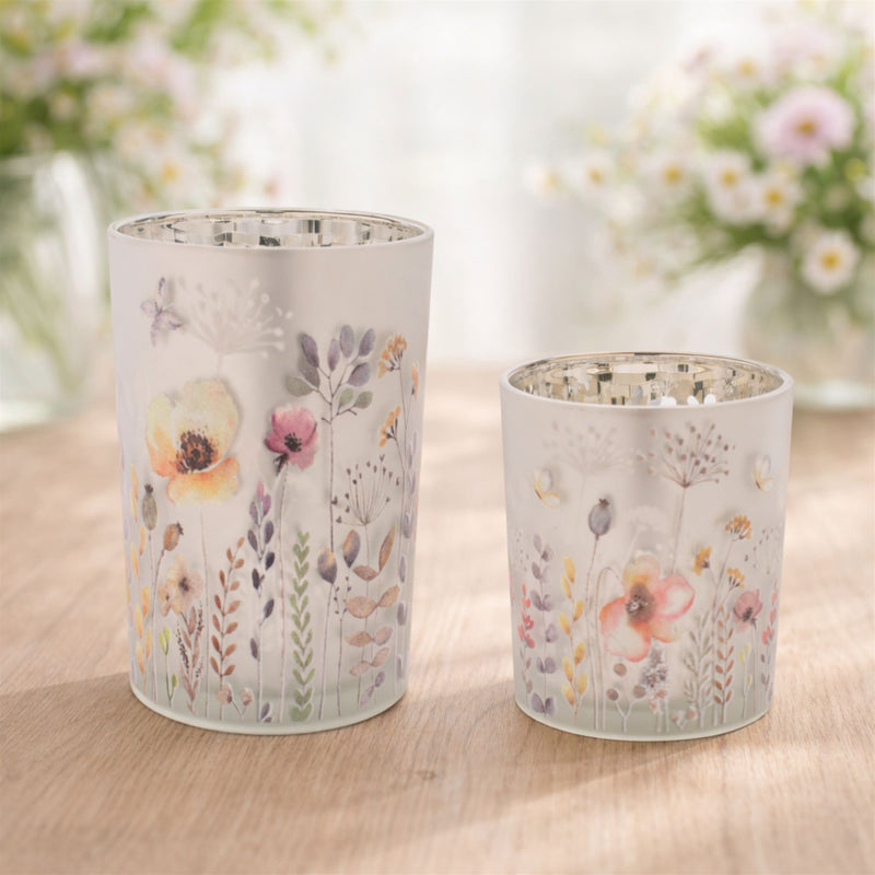 Two floral-patterned candle holders on a wooden surface with a blurred floral background.