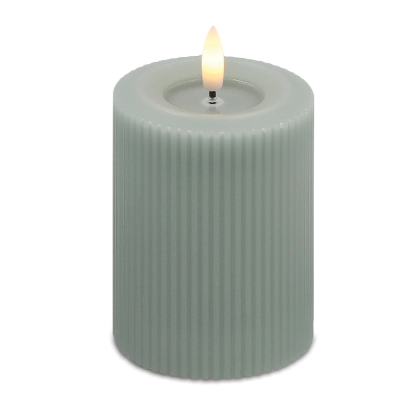 Green ribbed candle with a lit wick on a white background