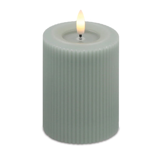 Green ribbed candle with a lit wick on a white background