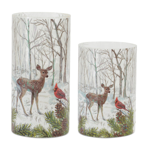 Two cylindrical candles with winter forest design featuring deer and cardinals on a white background.