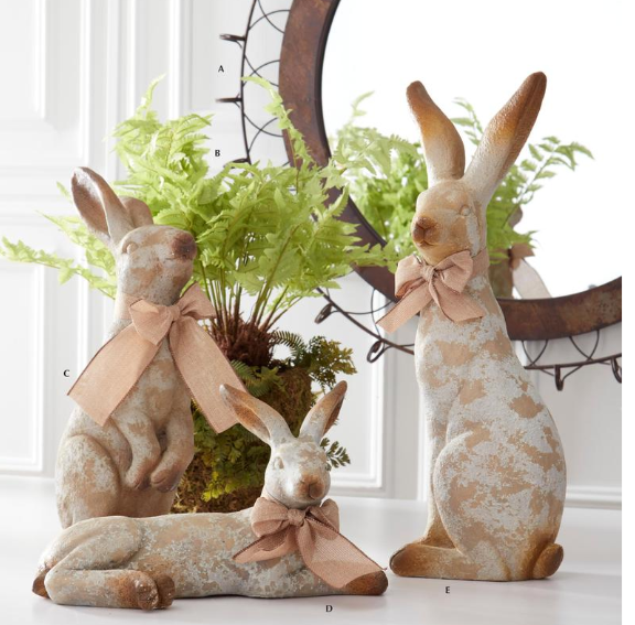 Three decorative rabbits with bows in a home setting with plants.