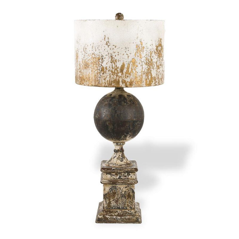 A distressed table lamp with a dark metallic spherical center, an ornate square pedestal base, and a drum shade featuring a white top that fades into gold at the bottom, set against a plain white background.