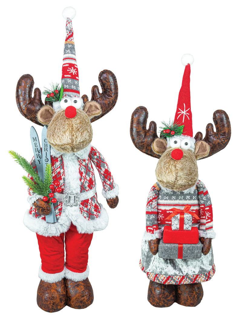 Two Christmas reindeer figurines on a plain white background. One wears a Santa-style outfit with red pants, a patterned sweater, and a tall striped hat while holding greenery and a silver object.