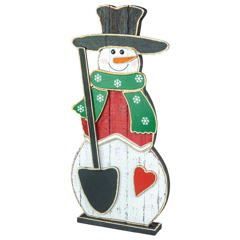 A decorative snowman figurine with a black top hat, green scarf with white snowflakes, red coat, white body, black shovel, and a red heart on a white background.