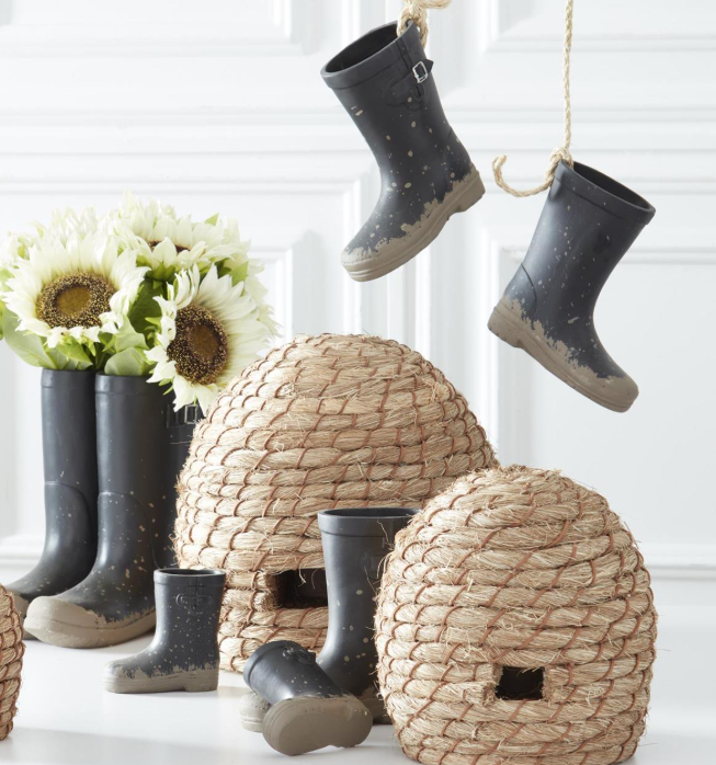Decorative display with black rain boots, woven baskets, and flowers on a white surface.