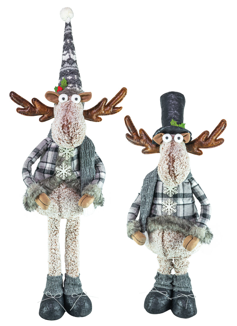 Two rustic Christmas reindeer figurines standing side by side on a plain white background. One reindeer wears a tall patterned hat and the other wears a tall black hat, both with plaid outfits, faux fur details, and knitted boots.