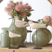 Decorative birds on stands with green vases and pink flowers in the background