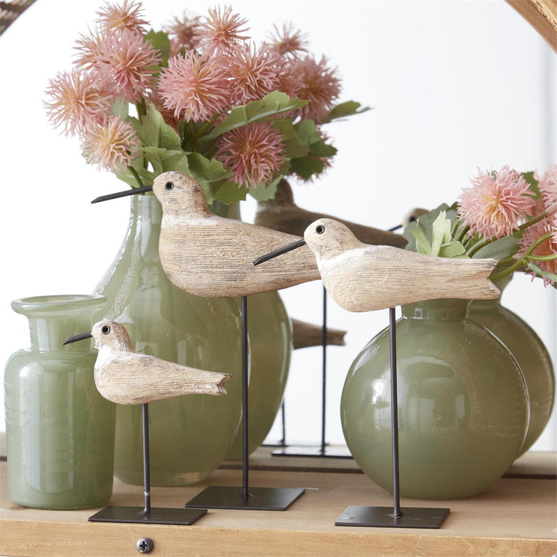 Decorative birds on stands with green vases and pink flowers in the background