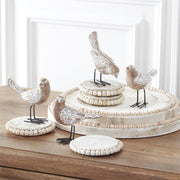 Decorative bird figurines on a wooden surface with a white wall background