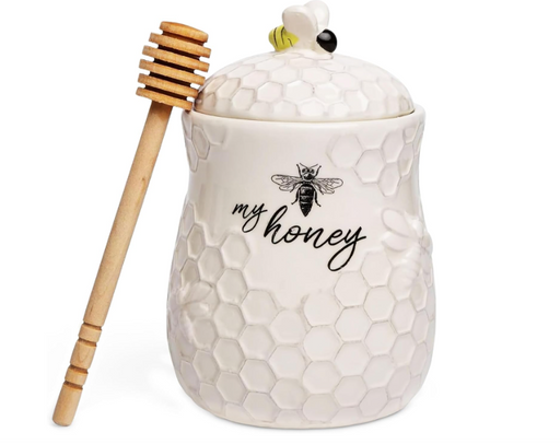 White honey jar with honeycomb design and a wooden dipper on a white background