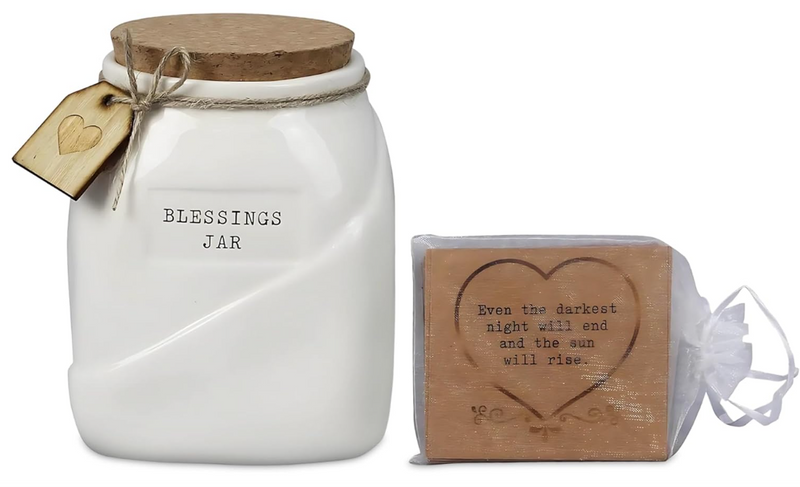 White blessings jar with wooden lid and tag, next to a small bag with a heart design and text.