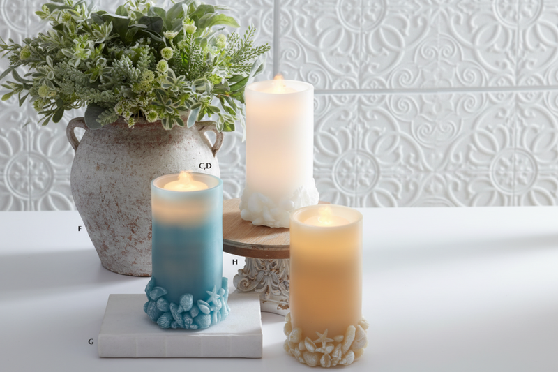 Decorative candles with textured bases on a white surface with a light gray textured wall background.