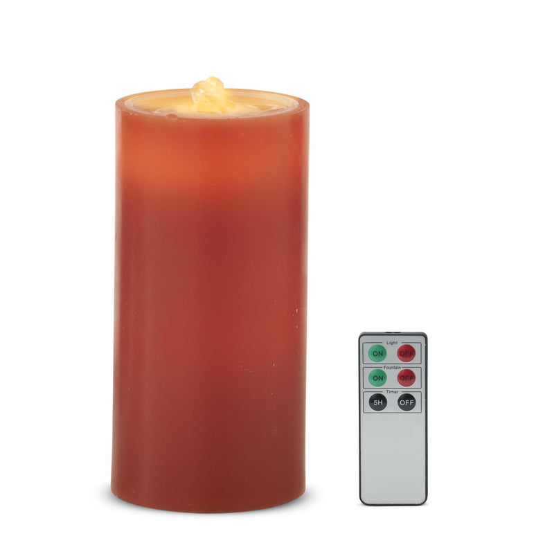 A red-orange cylindrical LED pillar candle with a faux flame on top, shown next to its silver remote control on a white background.