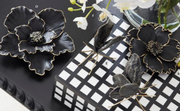 Black floral brooches on a checkered surface with flowers in the background