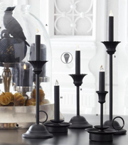 Set of black candle holders on a reflective surface with a blurred decorative background.