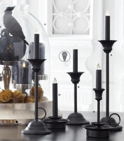 Set of black candle holders on a reflective surface with a blurred decorative background.