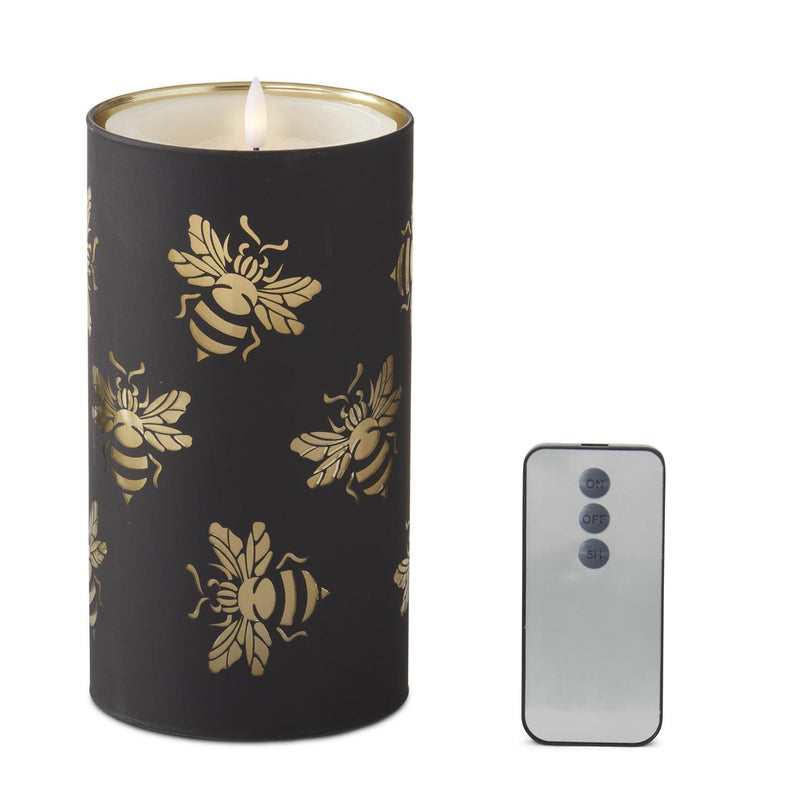 Black candle with gold bee patterns next to a smartphone on a white background