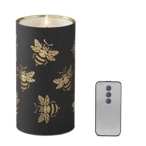 Black candle with gold bee patterns next to a smartphone on a white background