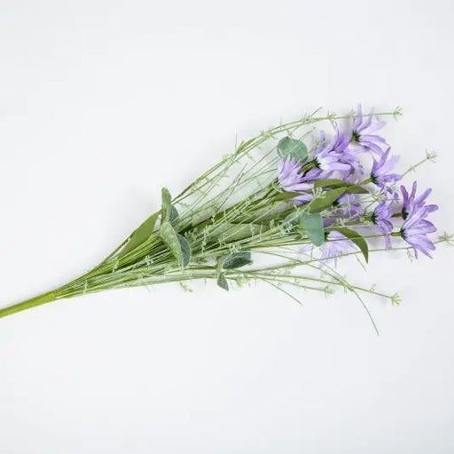 A bouquet of artificial purple flowers with green stems and leaves, laid diagonally on a plain white background.