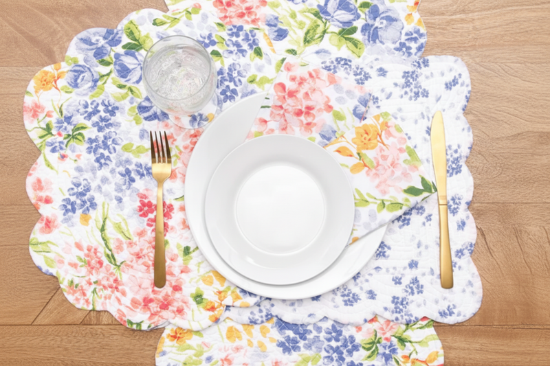Floral placemats with a white plate, fork, and knife on a wooden table.