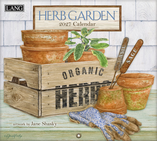 2027 Herb Garden calendar with gardening tools and wooden crate on a white brick background