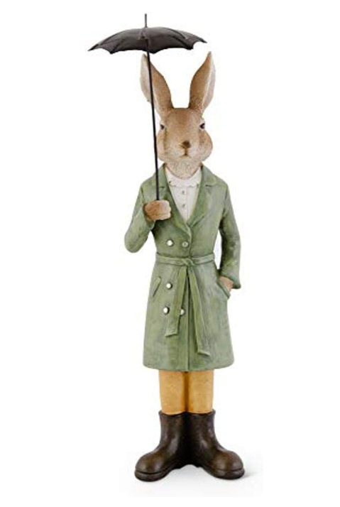Stuffed rabbit figure wearing a green raincoat and holding an umbrella on a white background