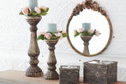 Decorative candle holders with flowers and candles on a table, reflected in a decorative mirror.