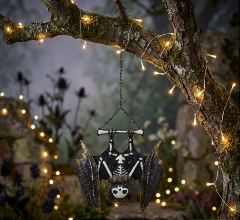 Decorative bat skeleton hanging from a branch with string lights in a mystical setting.