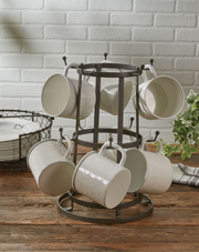 Set of white mugs on a metal stand against a brick wall.