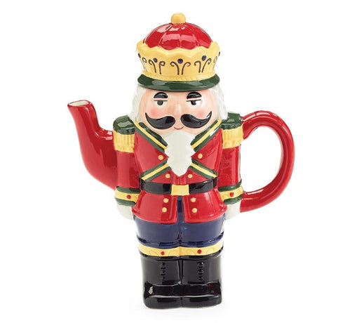 A ceramic nutcracker-shaped teapot featuring a red military uniform, gold trim, a white beard, black mustache, blue pants, and a red and gold crown, shown on a plain white background.