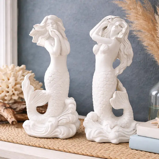 Two white mermaid figurines on a decorative surface with a neutral background