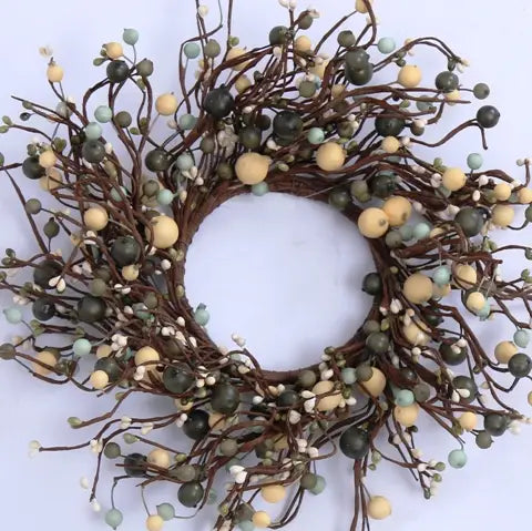 A decorative wreath made of brown branches with faux berries in muted green, pale blue, cream, and white, shown against a plain light background.