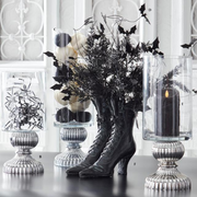 Decorative setup with black boots, candles, and foliage on a table.
