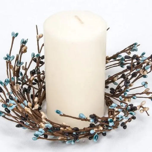 White candle in a decorative wreath with brown and blue branches on a white background
