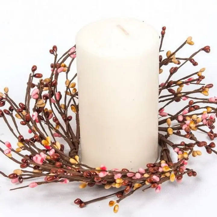 Decorative wreath with a white candle surrounded by small colorful berries on a white background