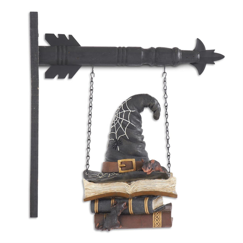 Decorative sign with a witch hat, books, and a cat on a swing, hanging from an arrow-shaped metal piece.