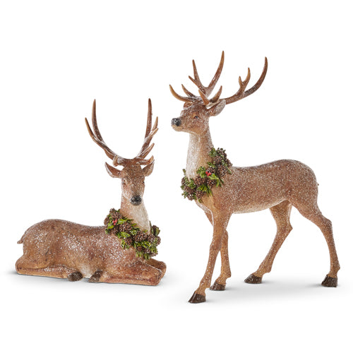 Two resin figurines of deer, one standing and one lying down, both adorned with glitter and wreaths.