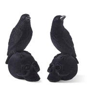 Two black velvet flocked crows perched on top of skull-shaped resin figurines.