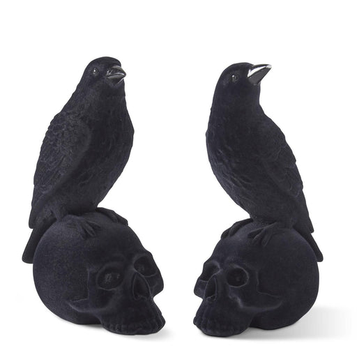 Two black velvet flocked crows perched on top of skull-shaped resin figurines.