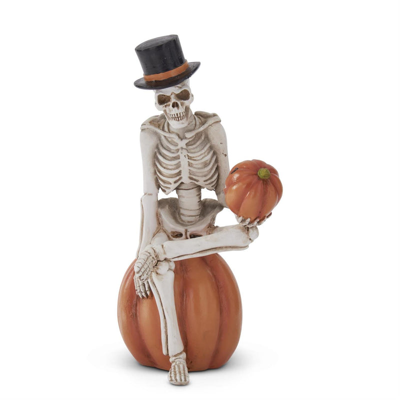 A skeleton figurine wearing a top hat and sitting on a pumpkin. The figurine is primarily white with a orange pumpkin and a brown hat.