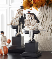 Decorative skeletons on black stands with pumpkins and a lace curtain in the background