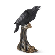 A black figurine of a perched crow sitting on a wooden stump.