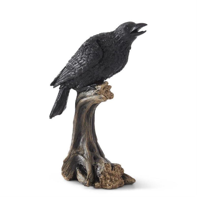 A black figurine of a perched crow sitting on a wooden stump.