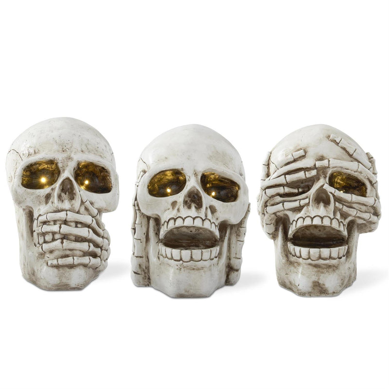 A set of three resin decorations shaped like skeleton heads with different facial expressions, painted in white and gold colors.