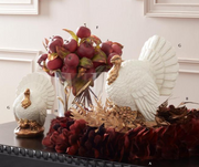 Decorative arrangement with apples, feathers, and a turkey figurine on a table.