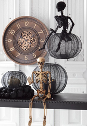 Decorative Halloween scene with skeletons and wire pumpkins on a shelf.
